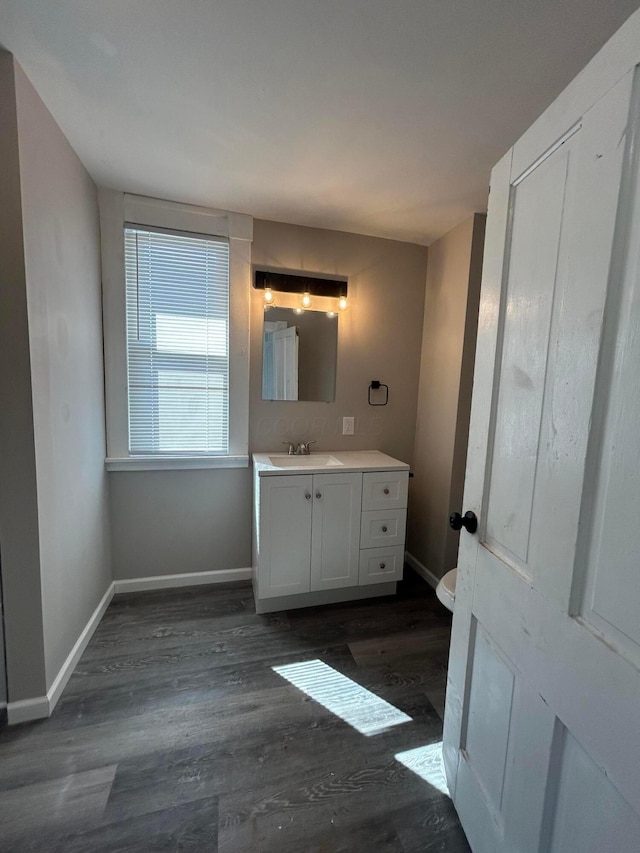 bathroom with toilet, wood finished floors, vanity, and baseboards