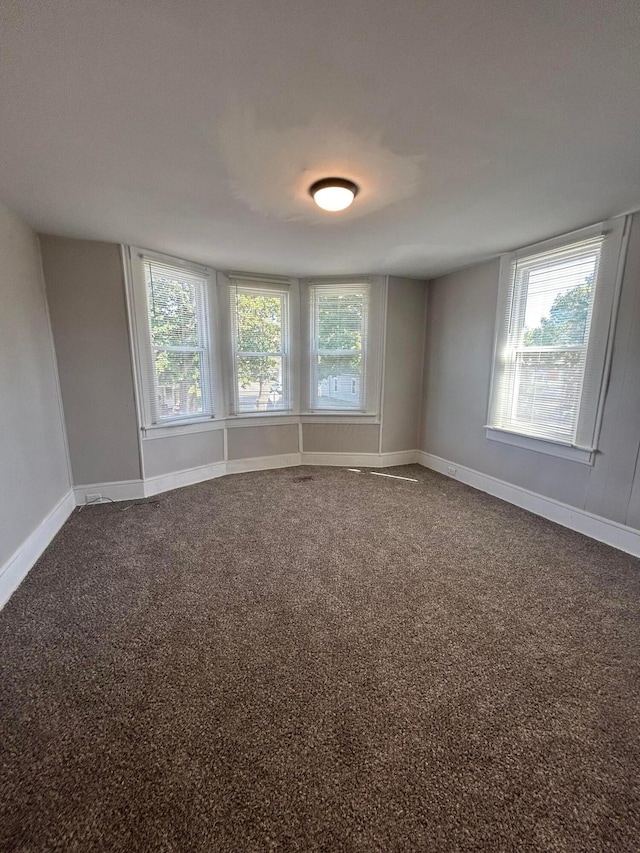 empty room featuring dark carpet, baseboards, and a healthy amount of sunlight