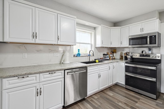 1779 Fairwood Ave, Columbus, OH 43207 - kitchen featuring a sink, appliances with stainless steel finishes, white cabinetry, light wood-style flooring, and light stone counters