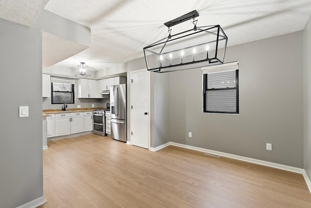 121 Granville St, Pataskala, OH 43062 - kitchen with light wood-type flooring, a textured ceiling, under cabinet range hood, appliances with stainless steel finishes, and a notable chandelier