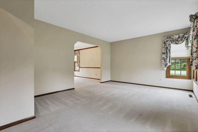 carpeted empty room with arched walkways, visible vents, and baseboards