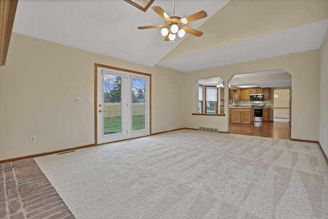 unfurnished living room with visible vents, baseboards, arched walkways, ceiling fan, and lofted ceiling