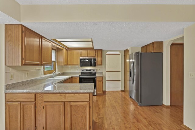 kitchen with light wood-type flooring, a sink, a peninsula, and stainless steel appliances