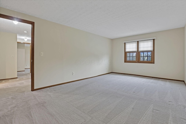 empty room with baseboards, light carpet, and a textured ceiling