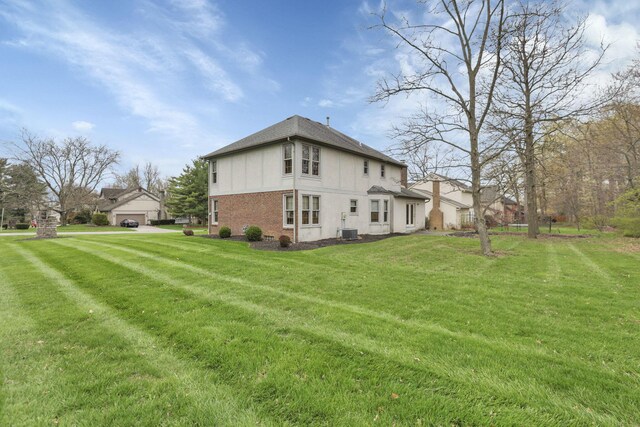 rear view of house featuring central air condition unit, stucco siding, a lawn, brick siding, and a garage