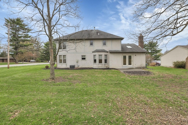 back of property with stucco siding, a chimney, a patio area, central AC, and a yard