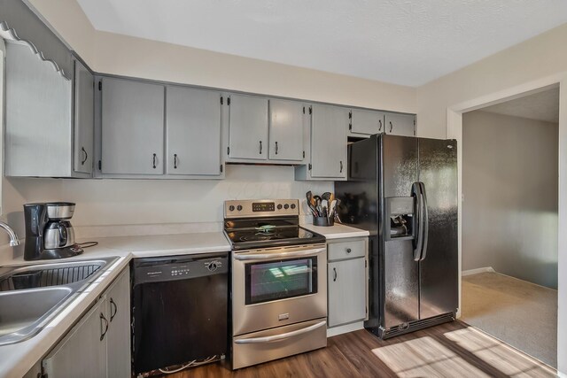kitchen featuring light countertops, a sink, dark wood-type flooring, gray cabinetry, and black appliances