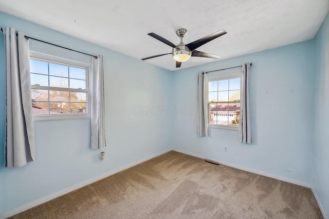 empty room featuring carpet floors, a ceiling fan, visible vents, and baseboards