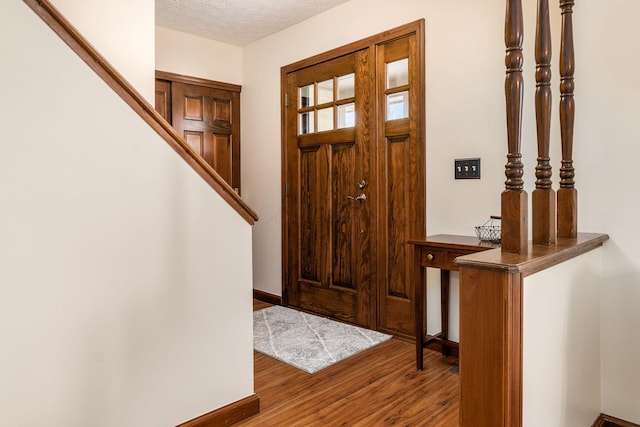 foyer entrance featuring baseboards, stairway, wood finished floors, and a textured ceiling