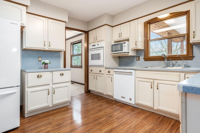 kitchen with light wood-type flooring, white appliances, white cabinetry, decorative backsplash, and a sink