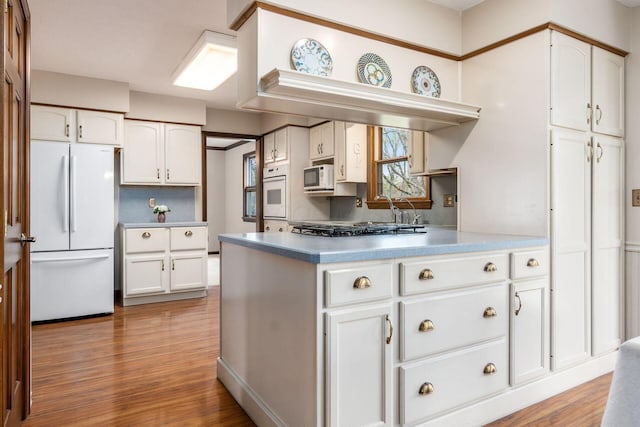 kitchen with white cabinetry, white appliances, and wood finished floors