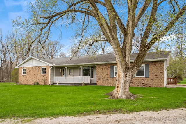 ranch-style house with a porch, roof with shingles, a front yard, and brick siding