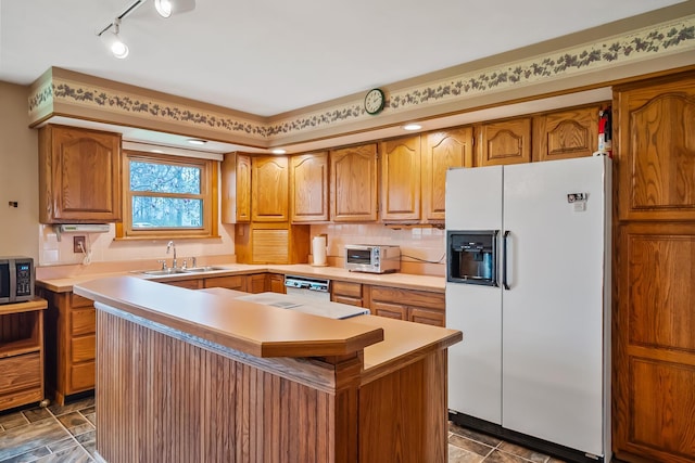 kitchen with a sink, light countertops, white appliances, brown cabinets, and rail lighting