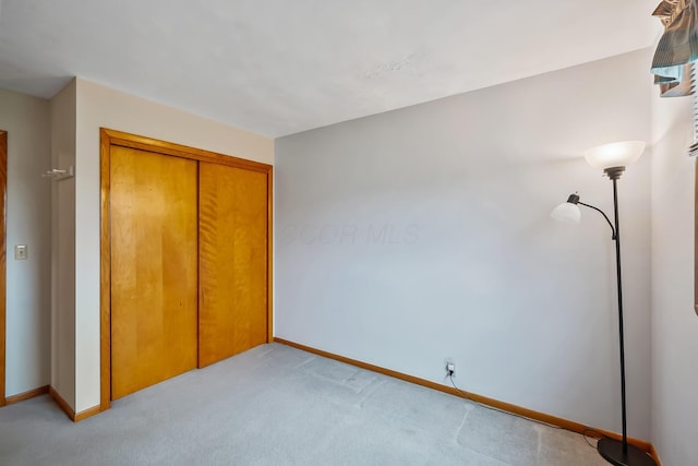 unfurnished bedroom with a closet, light colored carpet, and baseboards