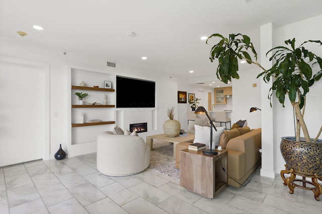 living area with visible vents, marble finish floor, a warm lit fireplace, recessed lighting, and built in shelves