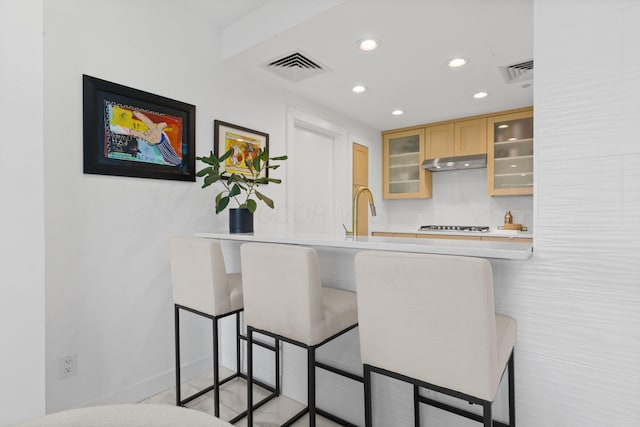 kitchen featuring visible vents, recessed lighting, under cabinet range hood, and glass insert cabinets