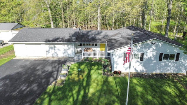 ranch-style home featuring a front yard, a wooded view, roof with shingles, and aphalt driveway