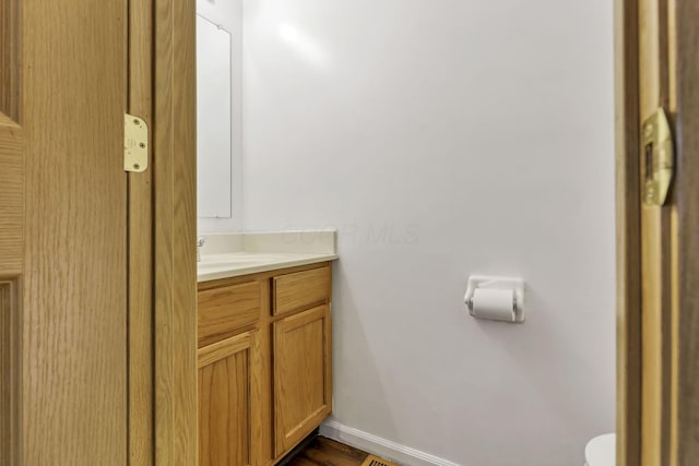 half bathroom with baseboards, wood finished floors, toilet, and vanity