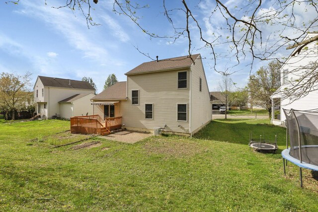back of property with a trampoline, a wooden deck, and a yard