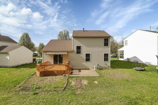 rear view of house featuring a deck, a fire pit, a yard, and roof with shingles