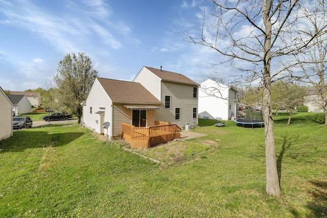 back of house featuring roof with shingles, a yard, a wooden deck, and a trampoline