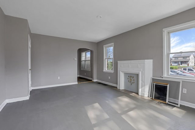 unfurnished living room with baseboards, arched walkways, and visible vents
