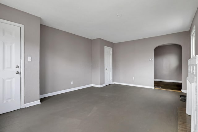 unfurnished living room featuring arched walkways, baseboards, and finished concrete flooring