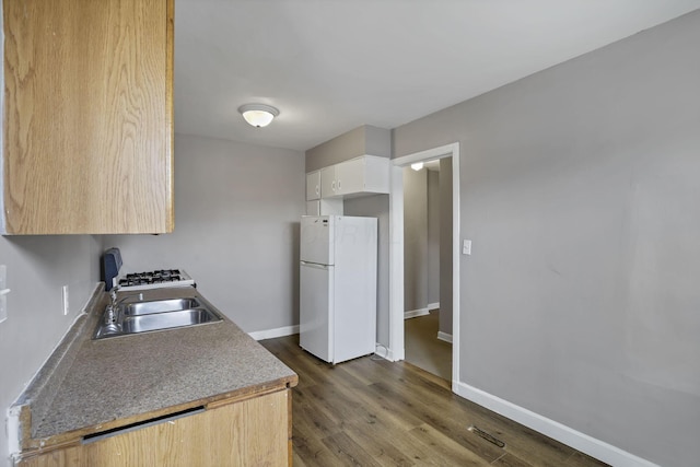 kitchen with white cabinets, a sink, freestanding refrigerator, baseboards, and dark wood-type flooring