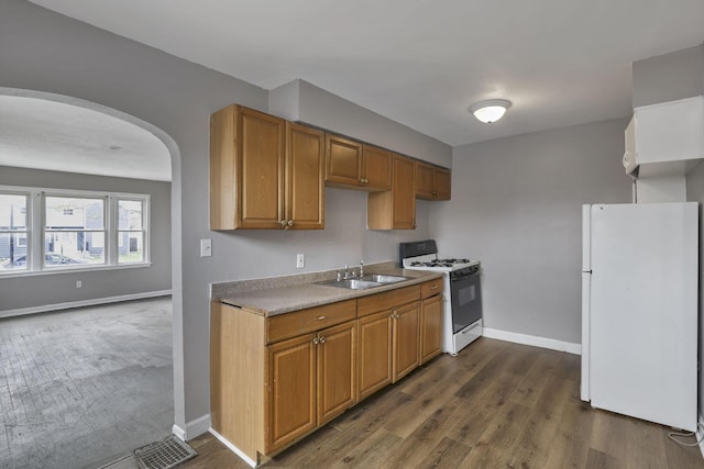 kitchen featuring gas range, arched walkways, dark wood finished floors, a sink, and freestanding refrigerator
