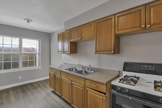 kitchen featuring wood finished floors, brown cabinetry, a sink, and gas range