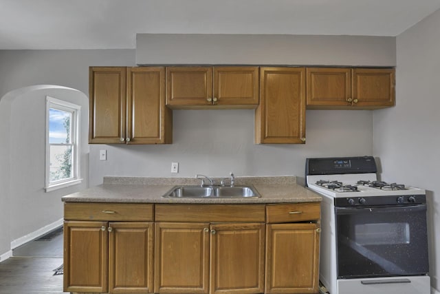 kitchen featuring brown cabinetry, dark wood finished floors, gas stove, baseboards, and a sink