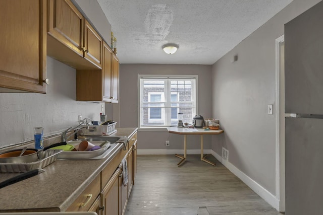 kitchen with brown cabinetry, a textured ceiling, visible vents, baseboards, and light wood-style flooring