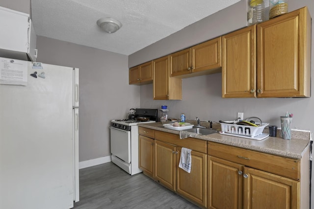 kitchen with brown cabinetry, white appliances, baseboards, a sink, and light wood-style flooring