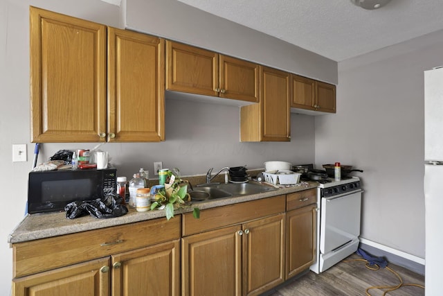 kitchen featuring white gas range oven, black microwave, a sink, baseboards, and wood finished floors