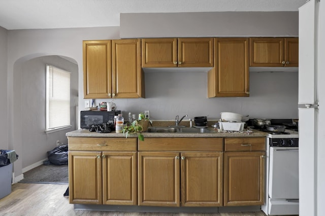 kitchen featuring black microwave, a sink, light wood finished floors, arched walkways, and gas range gas stove