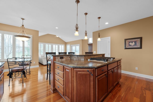 6700 Ballantrae Pl, Dublin, OH 43016 - kitchen featuring dark stone counters, brown cabinets, light wood-style floors, and a breakfast bar area
