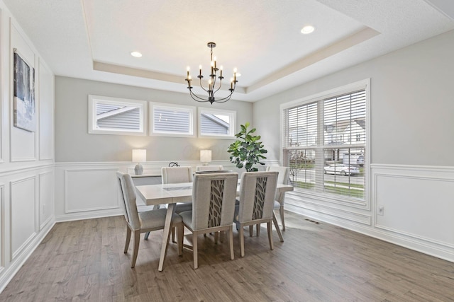 dining space with light wood-style floors, an inviting chandelier, recessed lighting, a wainscoted wall, and a raised ceiling