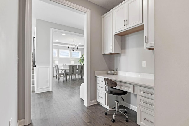 office area featuring built in desk, an inviting chandelier, and dark wood-style flooring