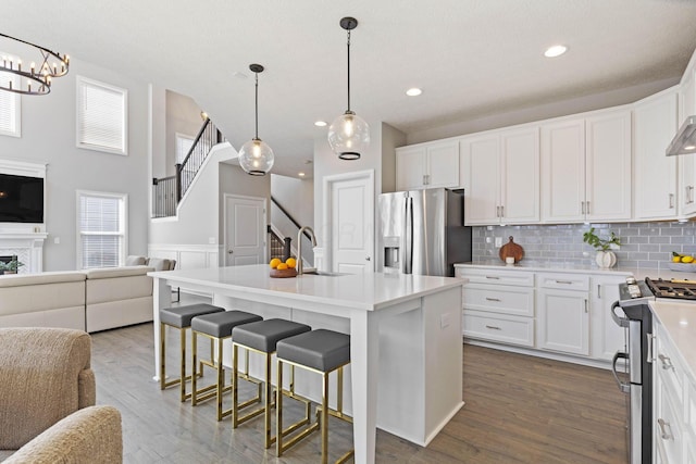 kitchen with a sink, open floor plan, dark wood-style flooring, appliances with stainless steel finishes, and backsplash