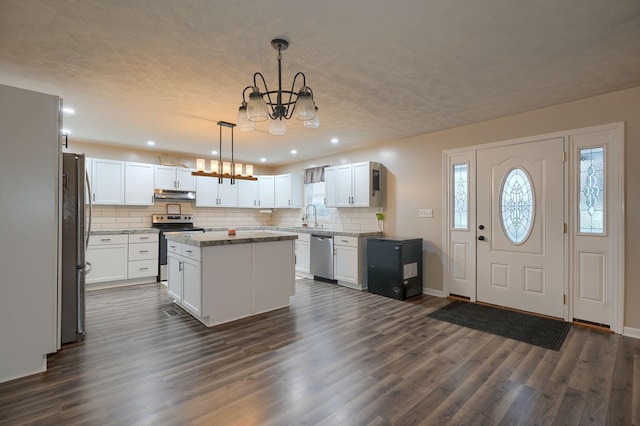 kitchen with a notable chandelier, under cabinet range hood, decorative backsplash, stainless steel appliances, and a sink
