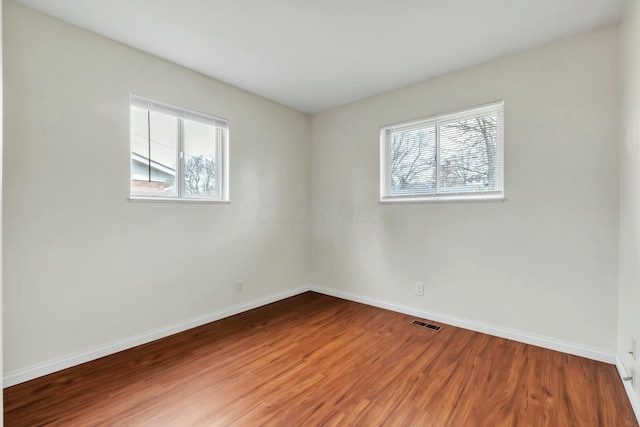 empty room with visible vents, baseboards, and wood finished floors