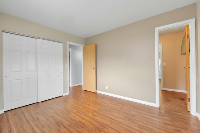 unfurnished bedroom with a closet, baseboards, light wood-type flooring, and visible vents