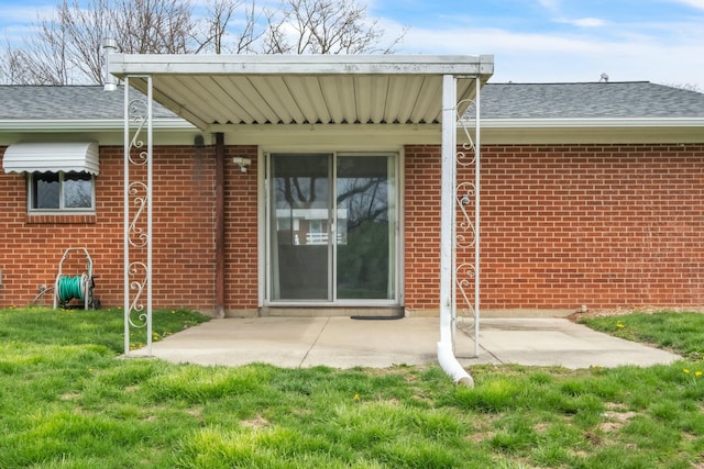 view of exterior entry with a shingled roof, a patio area, and brick siding