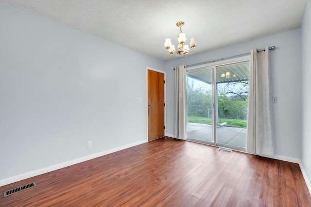 unfurnished room featuring a notable chandelier, visible vents, baseboards, and wood finished floors
