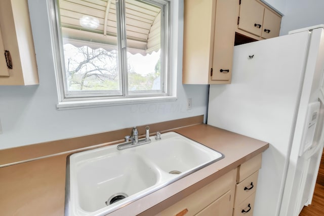 kitchen with light countertops, cream cabinets, white refrigerator with ice dispenser, and a sink