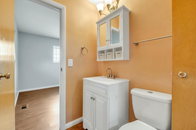 half bath with toilet, wood finished floors, vanity, and visible vents