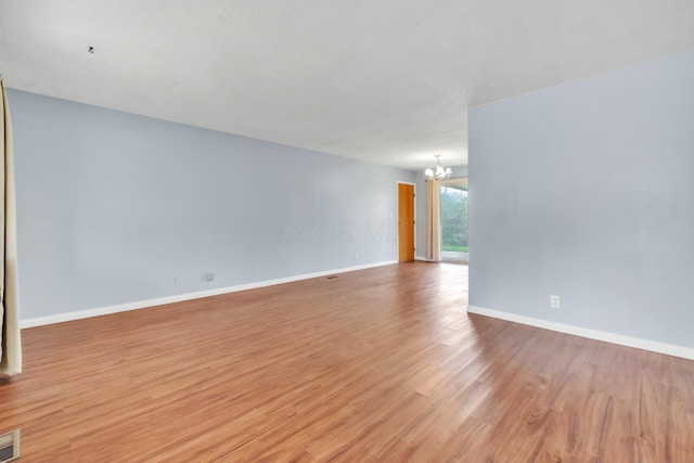 unfurnished room with light wood-style floors, an inviting chandelier, baseboards, and visible vents