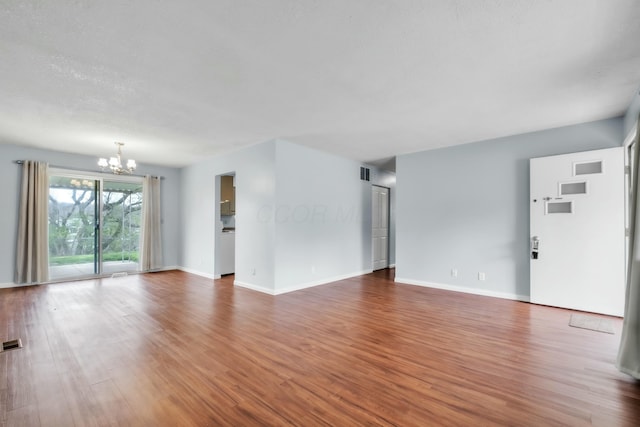 unfurnished living room featuring baseboards, wood finished floors, a notable chandelier, and visible vents
