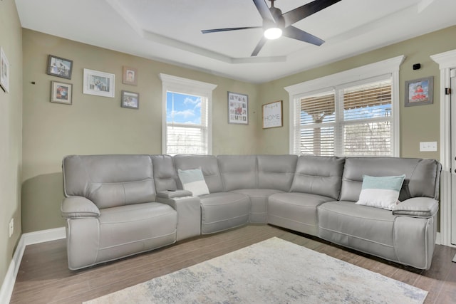 living room with ceiling fan, a raised ceiling, wood finished floors, and baseboards