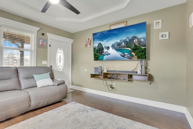 living area with a raised ceiling, baseboards, a ceiling fan, and wood finished floors